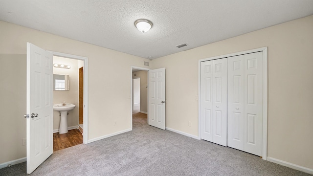 unfurnished bedroom featuring a textured ceiling, carpet floors, a sink, visible vents, and a closet