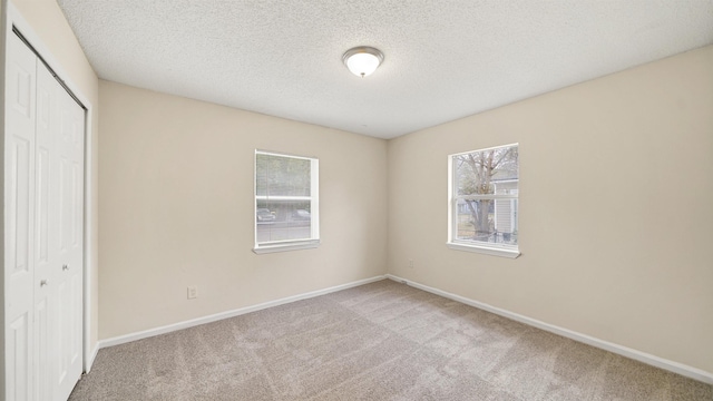 unfurnished bedroom with carpet floors, a closet, a textured ceiling, and baseboards