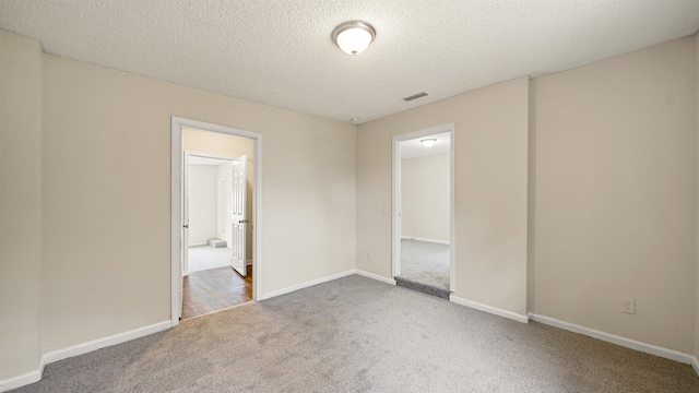 unfurnished bedroom featuring carpet, a textured ceiling, visible vents, and baseboards