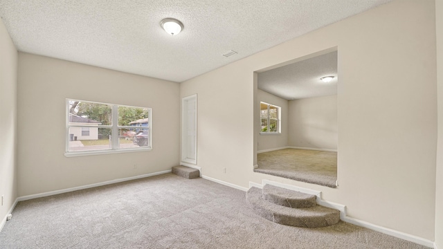 carpeted spare room featuring a textured ceiling, visible vents, and baseboards