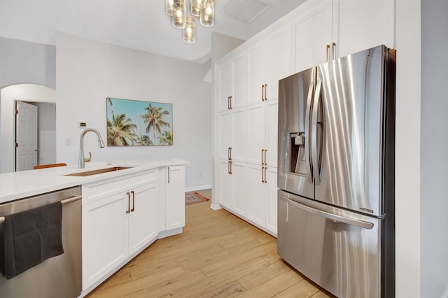 kitchen with appliances with stainless steel finishes, a sink, arched walkways, light wood finished floors, and white cabinets