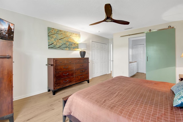 bedroom featuring light wood-style flooring, a closet, baseboards, a ceiling fan, and a barn door