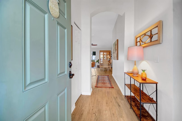 foyer entrance with light wood-style flooring, baseboards, and arched walkways