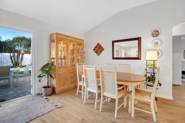 dining room featuring lofted ceiling, light wood finished floors, arched walkways, and baseboards