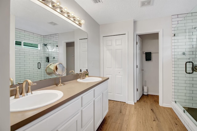 bathroom featuring wood finished floors, a shower stall, double vanity, and baseboards