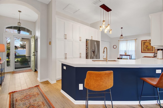 kitchen featuring stainless steel refrigerator with ice dispenser, a sink, a kitchen breakfast bar, white cabinets, and decorative light fixtures