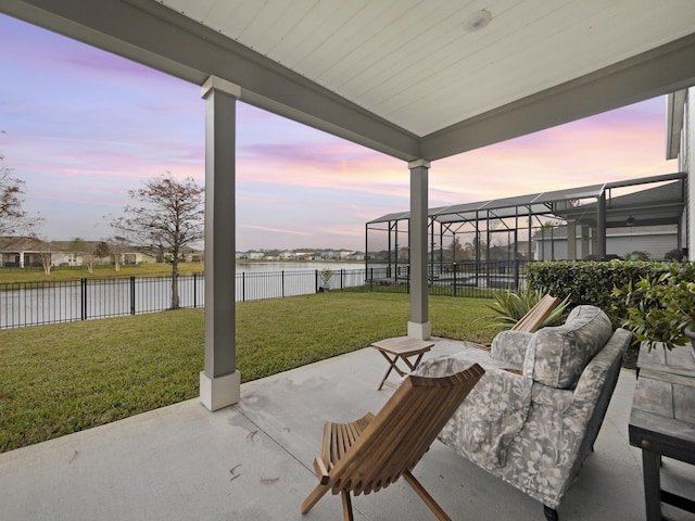 patio terrace at dusk featuring a lawn, glass enclosure, and a water view