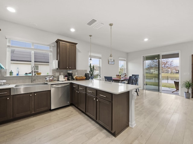 kitchen featuring sink, hanging light fixtures, stainless steel dishwasher, tasteful backsplash, and light hardwood / wood-style floors