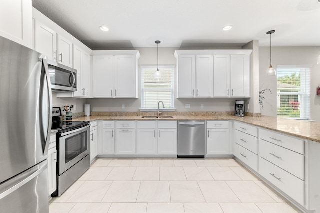 kitchen with a peninsula, plenty of natural light, a sink, stainless steel appliances, and white cabinetry