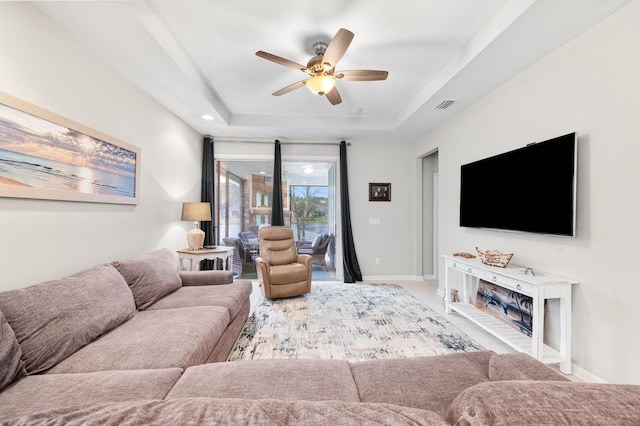 living room featuring a tray ceiling, baseboards, visible vents, and ceiling fan