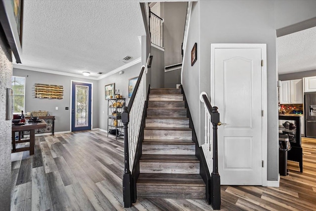 staircase featuring crown molding, wood-type flooring, and a textured ceiling