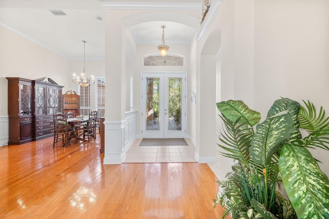 entrance foyer featuring an inviting chandelier, arched walkways, french doors, light wood-type flooring, and visible vents