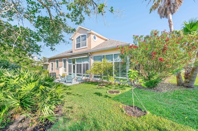 rear view of house with a lawn, stucco siding, a patio area, and roof with shingles