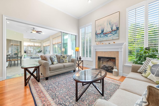 living area with crown molding, a tiled fireplace, wood finished floors, and ceiling fan
