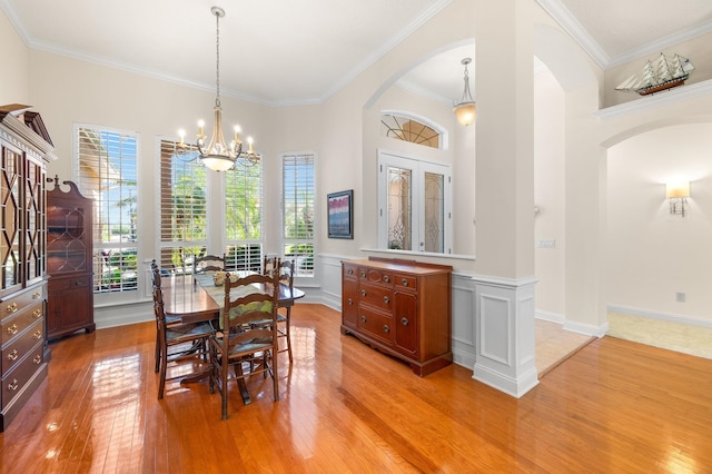 dining space with ornamental molding, light wood-style floors, a wainscoted wall, a chandelier, and arched walkways