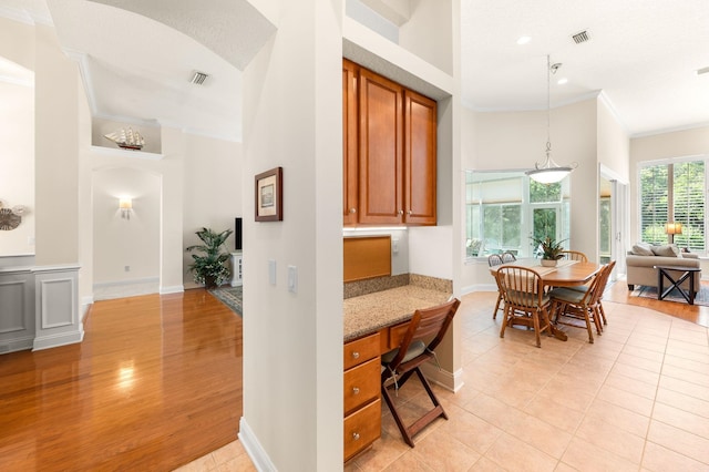 interior space featuring crown molding, light tile patterned flooring, a high ceiling, built in desk, and visible vents