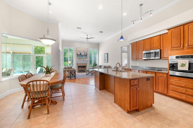 kitchen featuring crown molding, appliances with stainless steel finishes, brown cabinets, a fireplace with raised hearth, and open floor plan