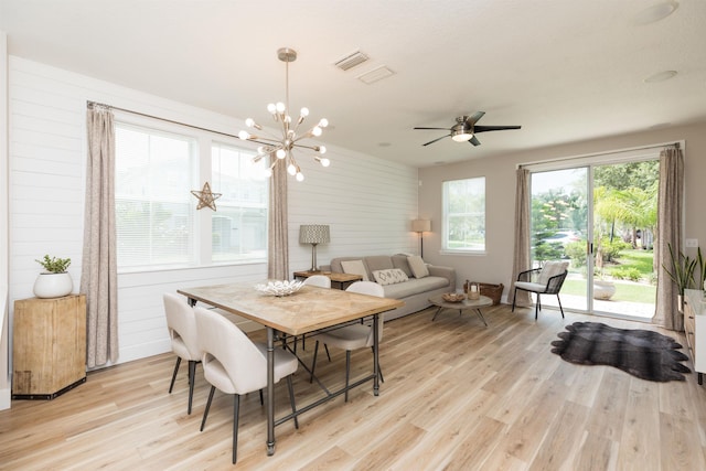 dining space featuring ceiling fan with notable chandelier, light wood-type flooring, and wood walls