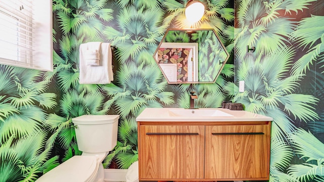 bathroom with vanity, toilet, and wallpapered walls