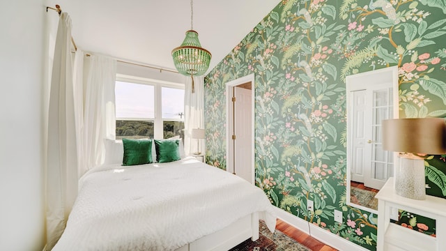 bedroom with wallpapered walls, baseboards, a chandelier, and wood finished floors