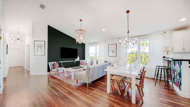 dining area with visible vents, vaulted ceiling, a notable chandelier, and wood finished floors