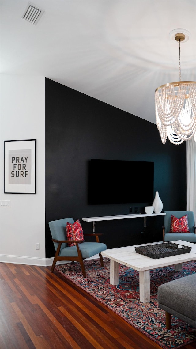 living area with an inviting chandelier, visible vents, baseboards, and wood finished floors