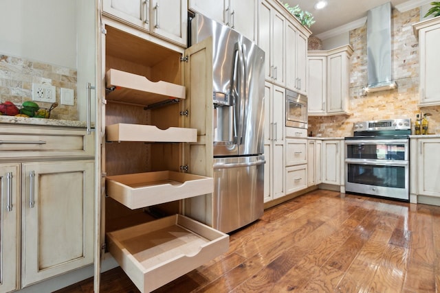 kitchen featuring wall chimney range hood, ornamental molding, tasteful backsplash, light hardwood / wood-style floors, and stainless steel appliances