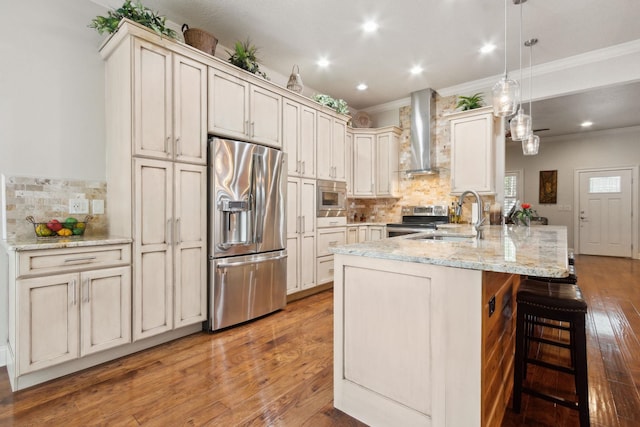 kitchen with sink, hanging light fixtures, stainless steel appliances, wall chimney range hood, and light stone counters