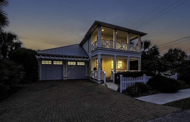 view of front of property featuring a balcony, fence, an attached garage, decorative driveway, and metal roof