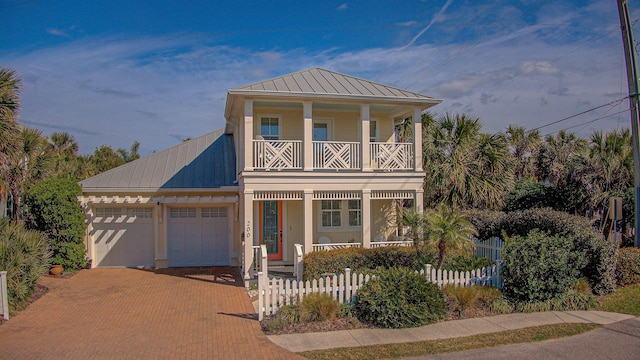 view of front of home featuring a fenced front yard, decorative driveway, an attached garage, metal roof, and a balcony