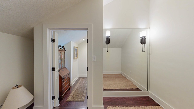 hall with a textured ceiling, wood finished floors, and vaulted ceiling