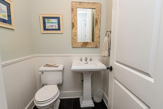 half bath with a sink, a wainscoted wall, toilet, and wood finished floors