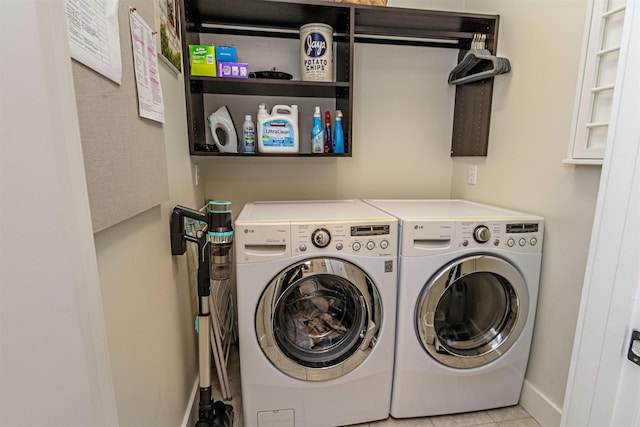 clothes washing area with laundry area, light tile patterned flooring, washing machine and dryer, and baseboards