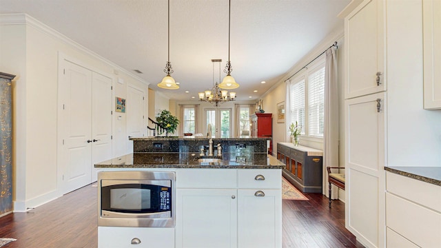 kitchen featuring dark stone countertops, an island with sink, dark wood-type flooring, crown molding, and stainless steel microwave