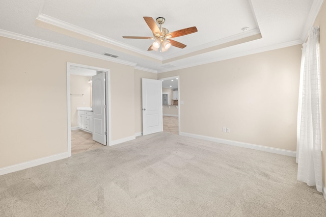 unfurnished bedroom with a raised ceiling, light carpet, ornamental molding, baseboards, and connected bathroom