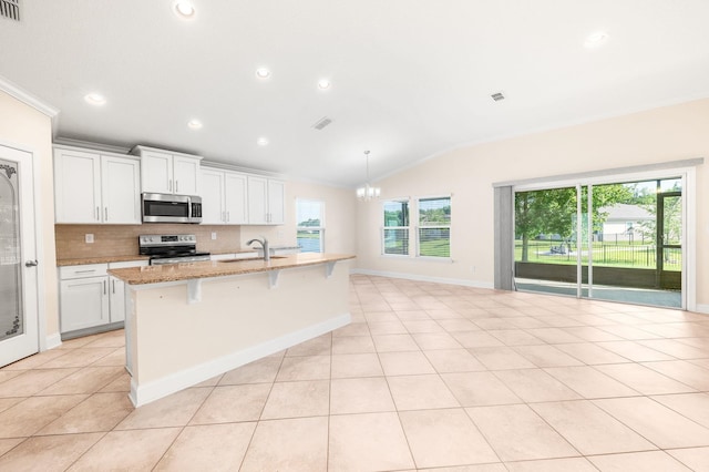 kitchen featuring stainless steel appliances, lofted ceiling, a center island with sink, backsplash, and light stone counters