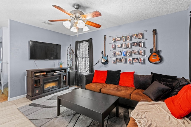 living room featuring ceiling fan, a fireplace, and a textured ceiling