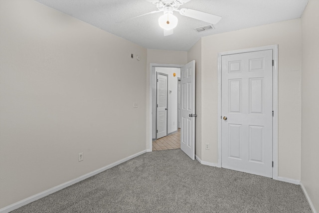 unfurnished bedroom featuring light carpet, a textured ceiling, and ceiling fan