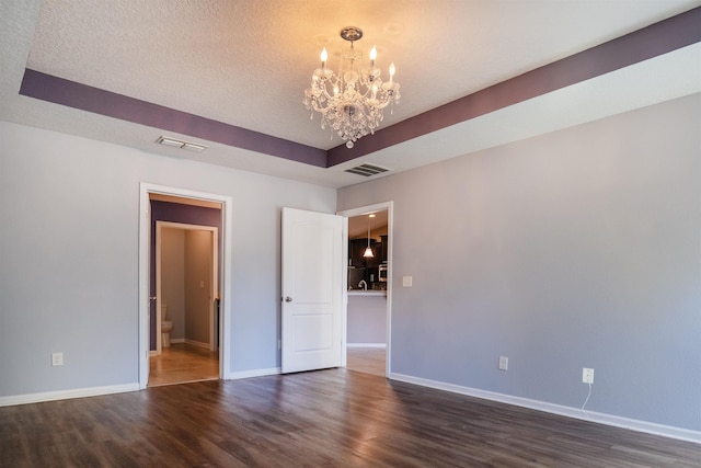 unfurnished room with a notable chandelier, dark hardwood / wood-style flooring, a textured ceiling, and a tray ceiling