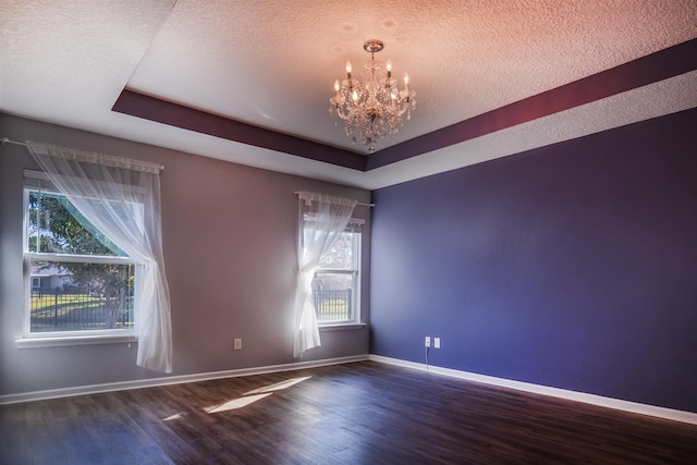 empty room with a raised ceiling, a textured ceiling, a chandelier, and dark wood-type flooring