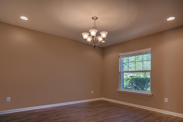 empty room featuring a textured ceiling, a chandelier, and dark wood-type flooring