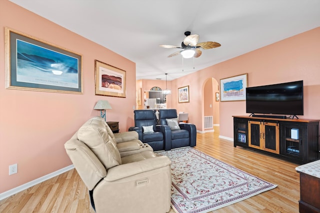 living area with light wood-type flooring, visible vents, arched walkways, and baseboards