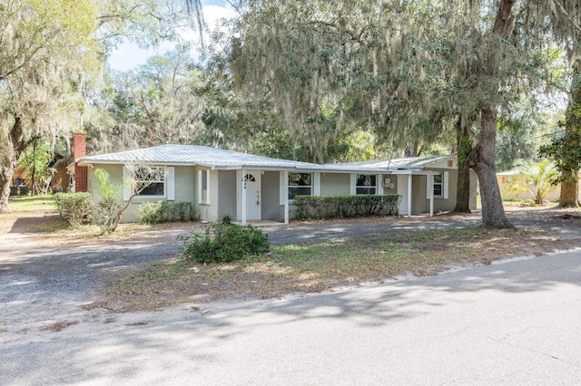 single story home featuring a chimney, metal roof, and stucco siding