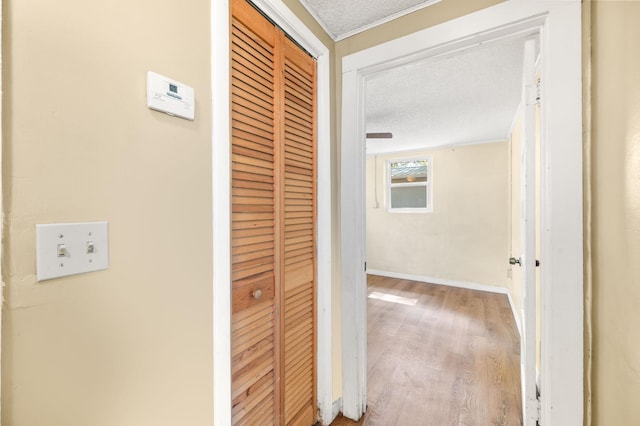 hallway featuring a textured ceiling, wood finished floors, and baseboards