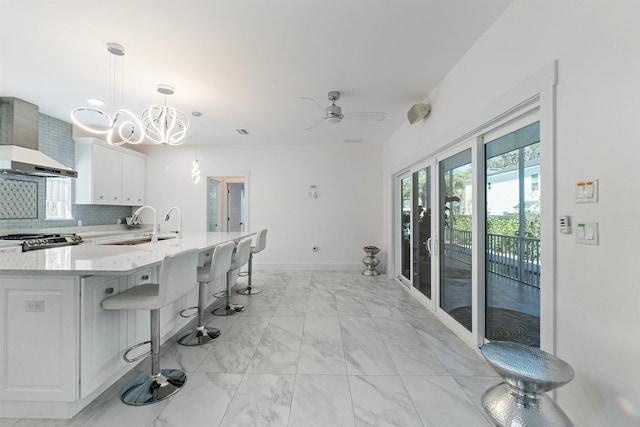 kitchen featuring stove, marble finish floor, wall chimney range hood, white cabinetry, and backsplash