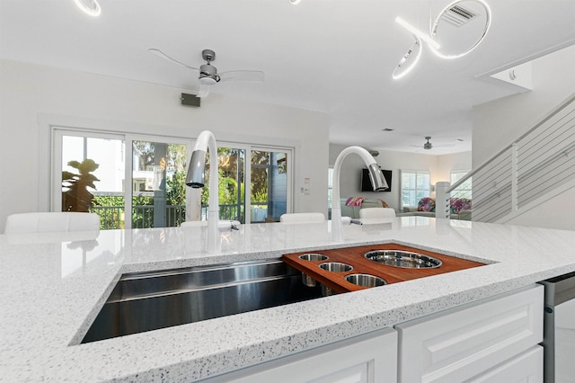 kitchen with a ceiling fan, open floor plan, light stone countertops, white cabinetry, and a sink