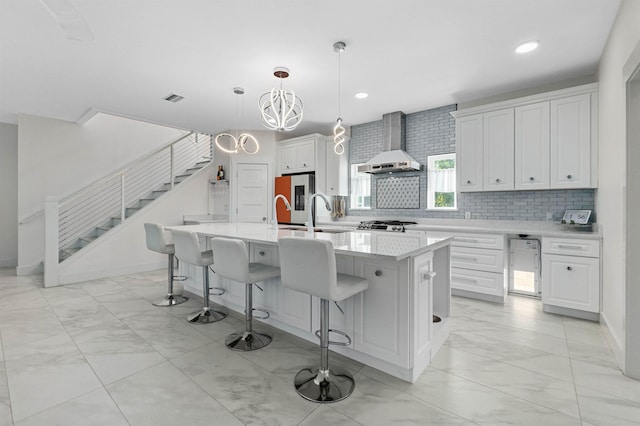 kitchen with visible vents, white cabinetry, light countertops, wall chimney exhaust hood, and an island with sink