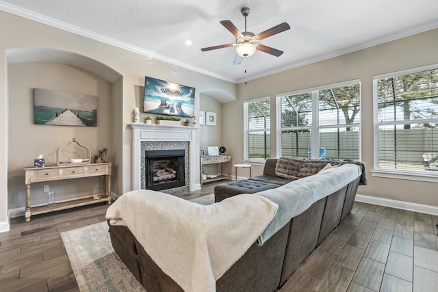 living room with a tiled fireplace, crown molding, ceiling fan, and a textured ceiling