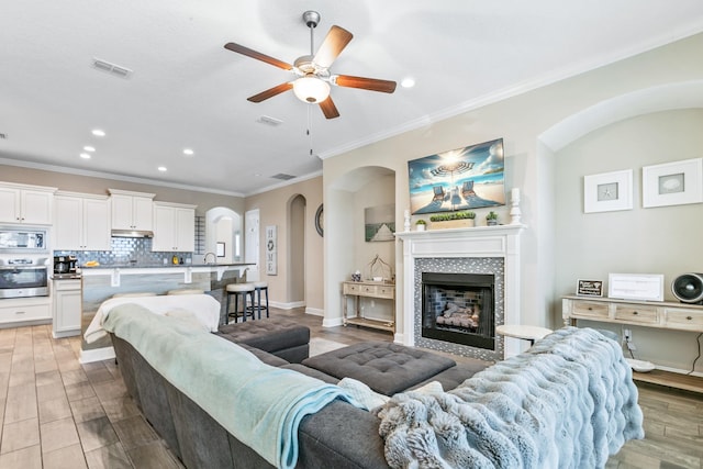 living room with ceiling fan, ornamental molding, a tiled fireplace, and light hardwood / wood-style flooring