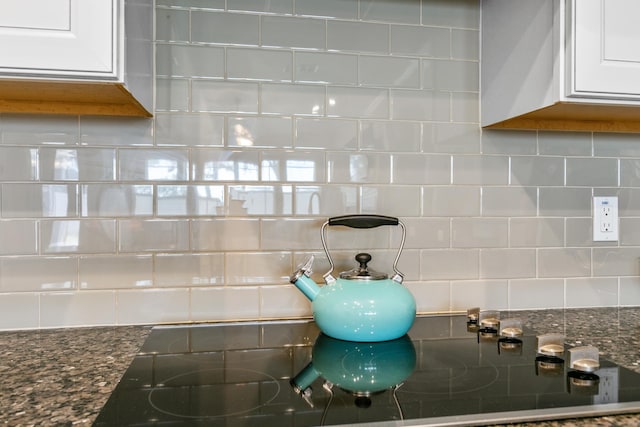 room details with tasteful backsplash, white cabinets, and dark stone counters